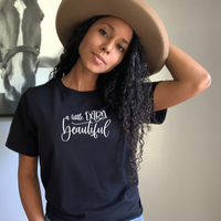 A woman wearing a black heather t-shirt with a little extra beautiful in white.
