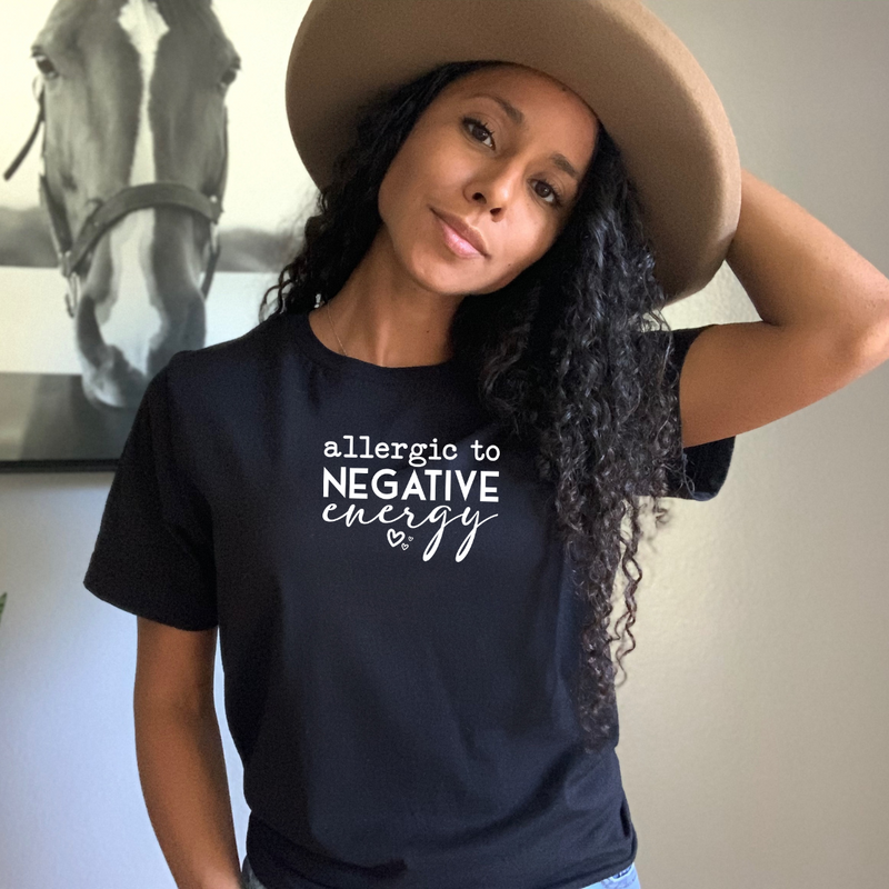 Woman wearing a black t-shirt with 'allergic to negative energy' text, standing indoors.