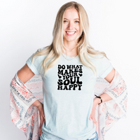 Woman wearing a light blue graphic t-shirt with bold retro lettering that reads "Do What Makes Your Soul Happy," styled with a lightweight floral kimono.