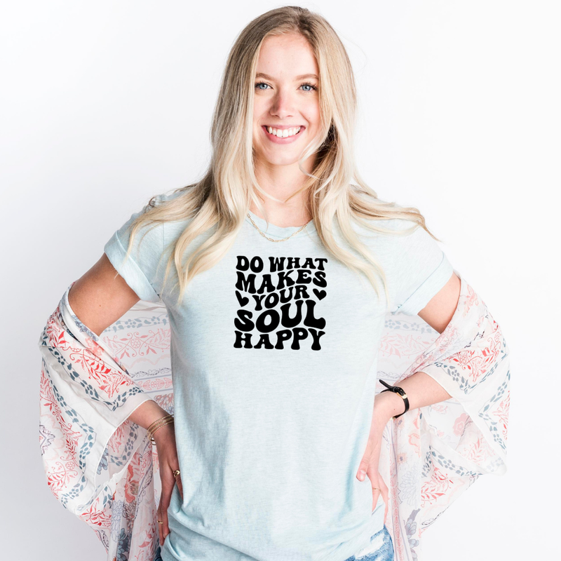 Woman wearing a Bella Canvas Heather Ice Blue t-shirt with text in retro-groovy font "Do what makes your soul happy" and a patterned kimono over her shoulders on a white background