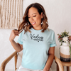 Woman wearing a light blue t-shirt with 'Kindness Matters' text, sitting in a chair.