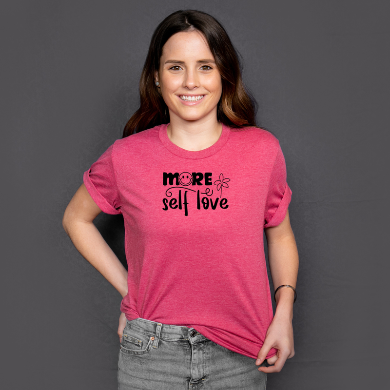 Woman wearing a pink t-shirt with 'More Self Love' text on a dark background