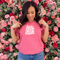 Woman wearing a Bella Canvas Raspberry t-shirt with white retro lettering that reads “Soul Full of Sunshine,” surrounded by cheerful flower illustrations.