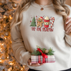 Woman wearing a Sand Gildan 81000 Crewneck Sweatshirt with a DTF image in red with text tis the season. The image includes Christmas Tree, gingerbread man, hot beverage, and a candy cane.
