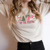Woman wearing a Sand Gildan 81000 Crewneck Sweatshirt with a DTF image in pink with text tis the season. Image includes hot beverage, Christmas Tree, gift with bow, santa hat.