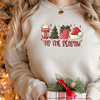 Woman wearing a Sand Gildan 81000 Crewneck Sweatshirt with a DTF image in red with text tis the season. Image includes hot beverage, Christmas Tree, gift with bow, santa hat. 