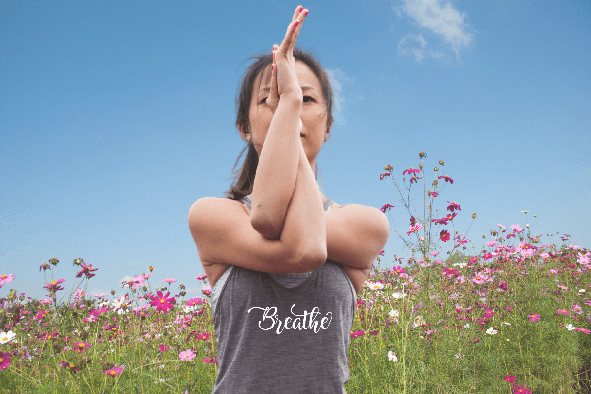 Woman in a yoga pose wearing a gray tank top with white script lettering "Breathe"