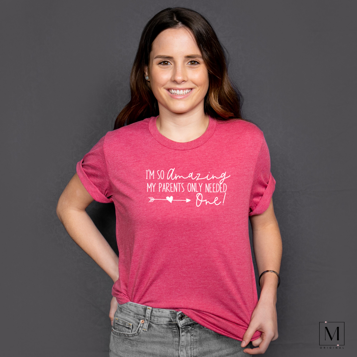 A young woman wearing a Heather Raspberry Bella Canvas 3001cvc t-shirt with white lettering reading I'm so amazing my parents only needed one! Part of Moxie Momma's exclusive only child line.