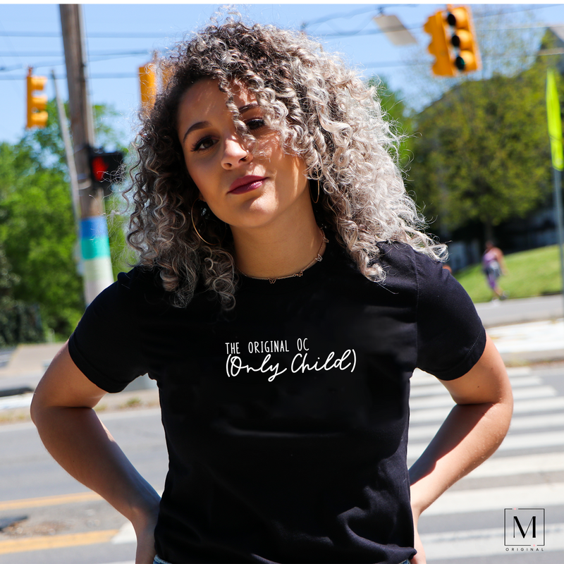 A woman wearing a Bella Canvas t-shirt in Heather black with The original OC (only child) in white lettering. Part of Moxie Momma's exclusive only child line.