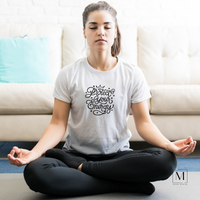 A young woman meditating wearing a white Bella Canvas tee with Protect your energy handwritten in black print/script.