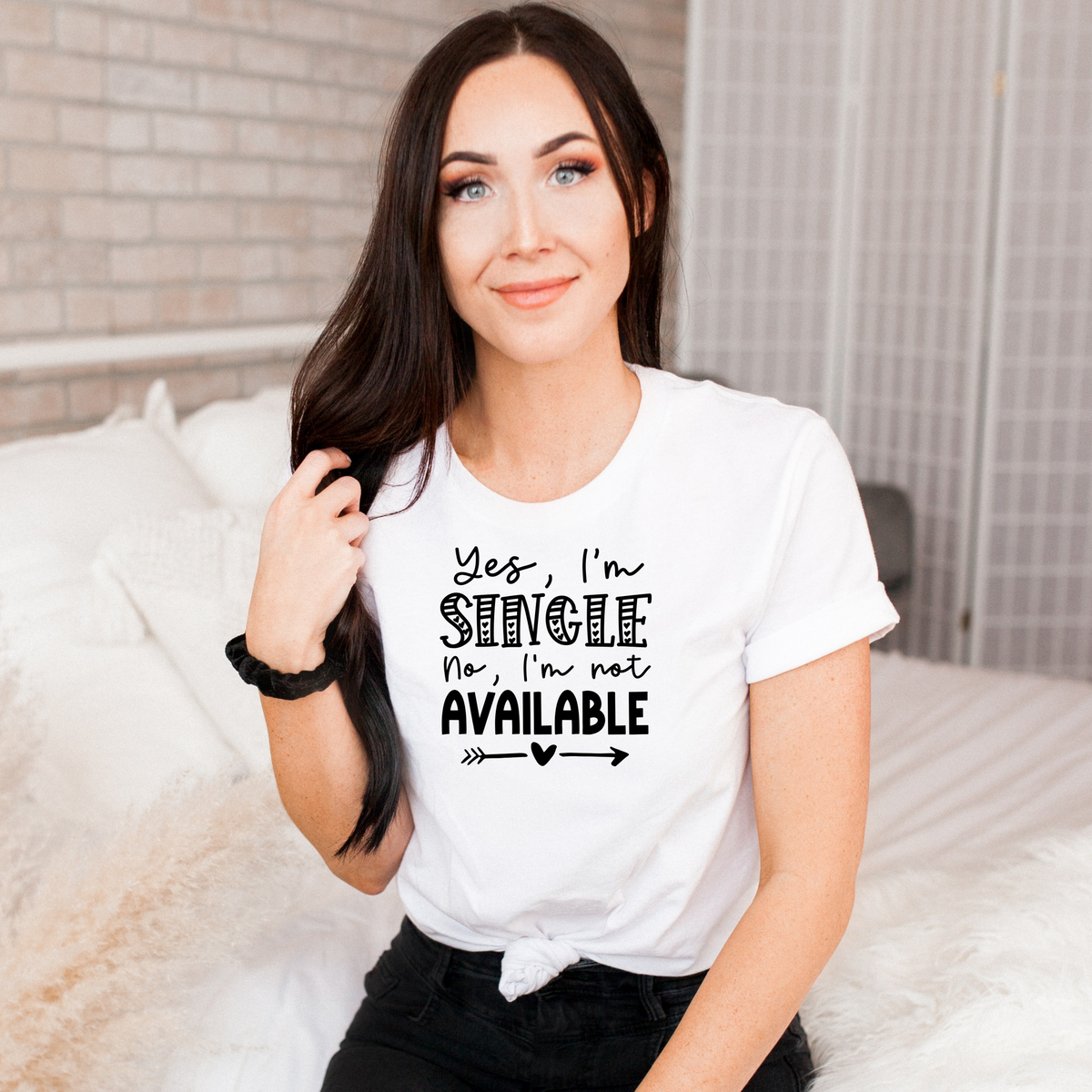 A woman wearing a Bella Canvas White tee with black lettering reading Yes, I'm single, No I'm not available. Part of Moxie Momma's Anti-Valentine's Day tees.