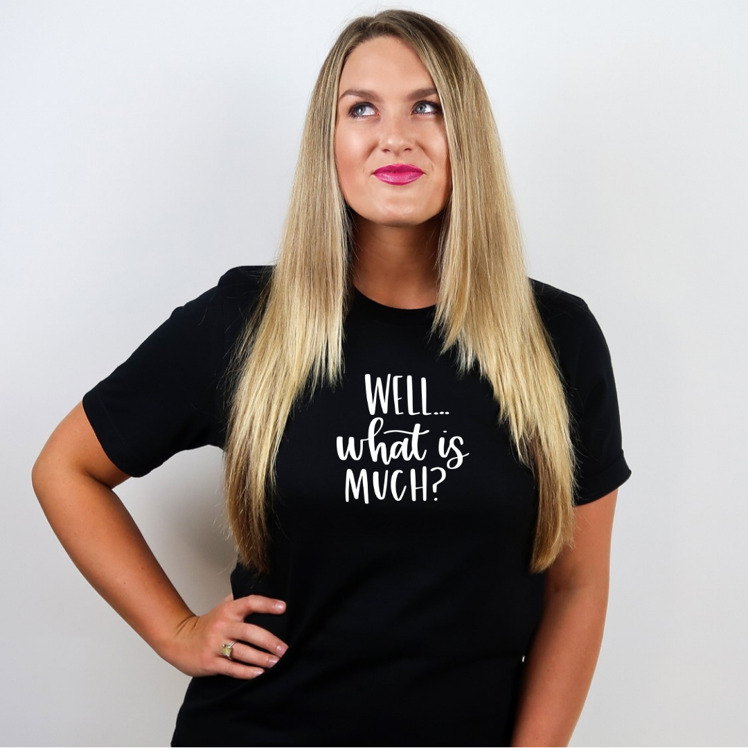 A woman wearing a black heather 3001cvc tee with Well..what is much? in white lettering.