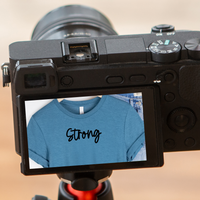 A camera with screen displaying the t-shirt as a reflection with the text reading Strong.
