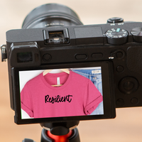 A camera with screen displaying the t-shirt as a reflection with the text reading Resilient.