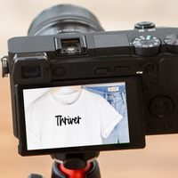 A camera with screen displaying the t-shirt as a reflection with the text reading Thriver..